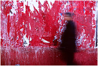 Ad Wall, Walking Figure: Madrid, Spain (2006) - Abstract photo of a red wall and a blurry walking man with an accusing stare