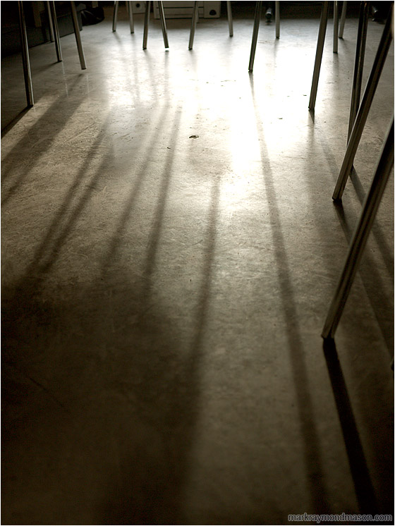 Chair Legs, Concrete Floor: Calgary, AB, Canada (2010-02-12) - Abstract photograph of intertwined chair legs, silhouetted in a pool of light on a concrete floor