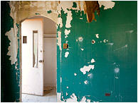 Doorways, Pockmarked Wall: Near Kamloops, BC, Canada (2012) - Fine art photograph of an archway and a slack door, set behind a peeling, pitted, bizarrely painted wall