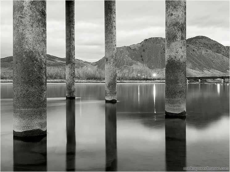 Concrete Piles, Rushing Water: Kamloops, BC, Canada (2012-12-01) - Fine art black and white photograph of large piles rising out of the frame from the smooth water of a full river