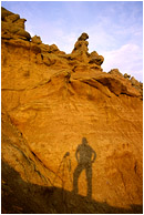 Self Portrait With Camera Shadow: Near Kamloops, BC, Canada (2002) - Landscape photograph of a silhouetted photographer and camera mounted tripod against a dramatic sculpted hoodoo background