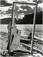 Door Frame, Rocky Beach: Shuswap Lake, BC, Canada (2016) - Fine art black and white photograph of a disembodied standing door with no walls and a beautiful background of lake, sky and mountains