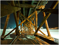 Beams, Ice, Night Sky: Salmon Arm, BC, Canada (2016) - Fine art photograph showing giant beams on the underside of a wharf, frozen in ice, set against a night sky with faint stars