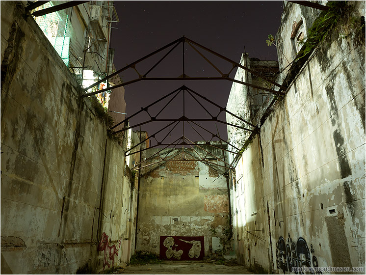 Graffiti, Steel Trusses, Night Sky: Havana, Cuba (2017-02-14) - Fine art photograph showing a vacant urban canyon between concrete buildings, with exposed trusses against a starry sky