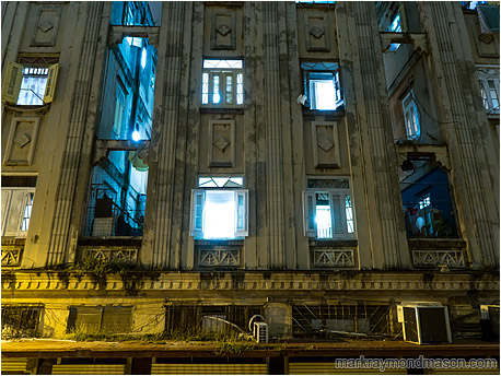 Fine art photograph showing windows open to the night and spilling blue light into the arc-sodium lit streets
