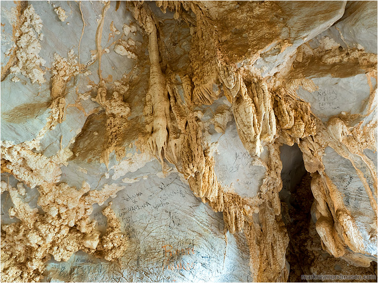 Cave Ceiling, Graffiti: Near Vinales, Cuba (2017-02-24) - Abstract photo showing popcorn rock and stalactites on the roof of a cave, with black charcoal graffiti all around