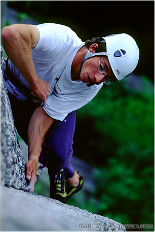 Climbing photo of a climber scaling a granite slab, high above the shaded forest floor