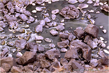 Fine art photograph showing water flowing around river rocks at the bottom of a basalt canyon