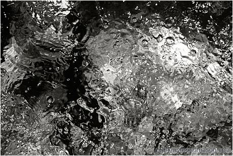 Abstract black and white photograph of the bubbling surface of a mountain creek, rendered in contrasted shades of grey