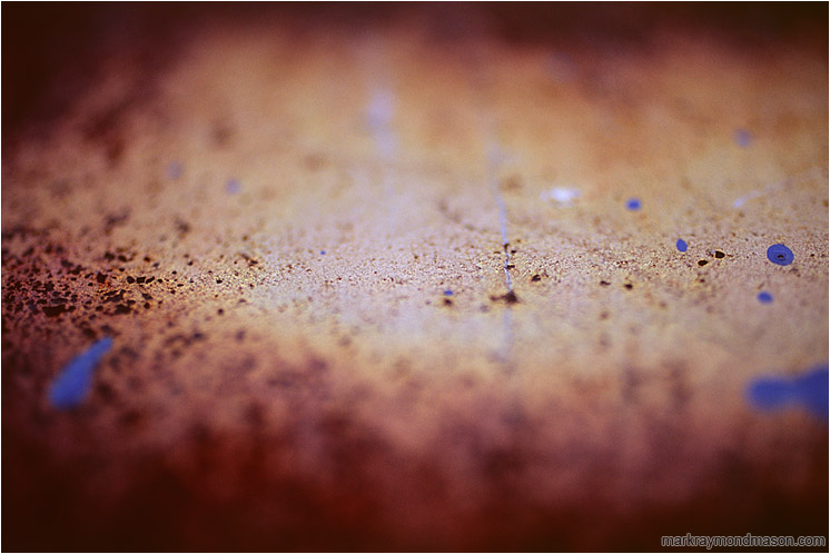 Rusted Steel, Paint Drops: Calgary, AB, Canada (2007-00-00) - Abstract photograph of blue paint splatter seeming to hover above a blurry, rusted steel plate