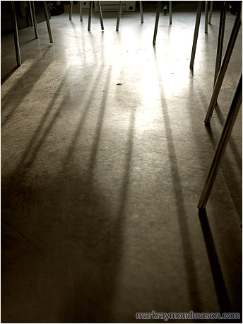 Abstract photograph of intertwined chair legs, silhouetted in a pool of light on a concrete floor