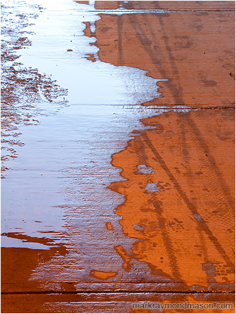 Abstract photo of a red concrete walkway covered in ice, water and tire tracks