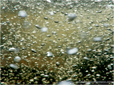 Abstract underwater photograph showing bubbles like mercury rising from the dark depths of a mountain creek