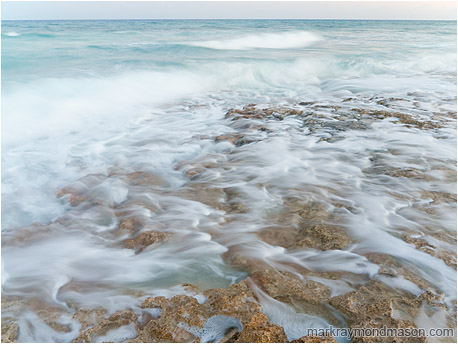 Fine art photograph of waves crashing on a limestone island, smokey and blurred by a long exposure