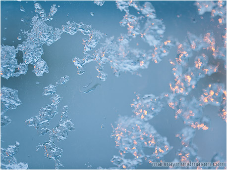 Abstract photograph of ice clinging to a window pane, lit by both natural and artificial light