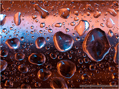 Fine art macro photo showing colourful reflected gradients and interlocking water drops on a curved piece of scrap steel