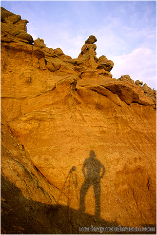 Landscape photograph of a silhouetted photographer and camera mounted tripod against a dramatic sculpted hoodoo background