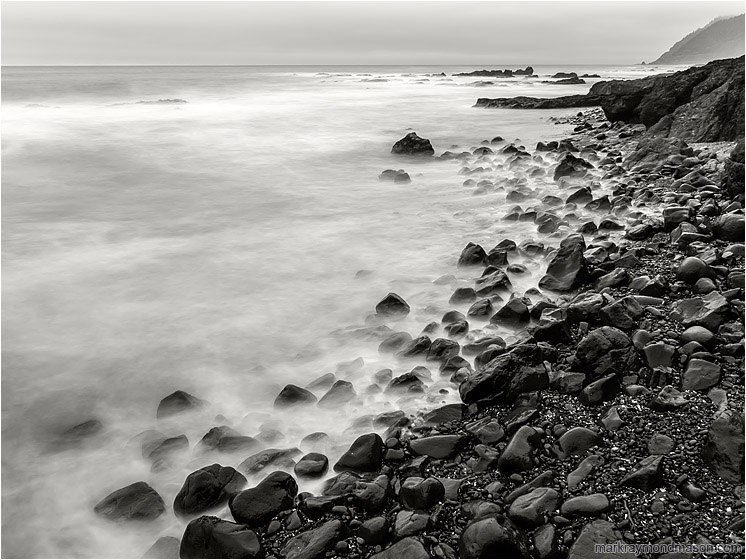 Rocky Beach, Smokey Waves: Near Stawberry Hill Park, OR, USA (2015-10-21) - Long exposure black and white photo of water crashing and receding on a beach littered with shiny rocks