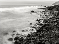 Rocky Beach, Smokey Waves: Near Stawberry Hill Park, OR, USA (2015) - Long exposure black and white photo of water crashing and receding on a beach littered with shiny rocks