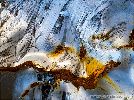 Abstract photograph showing painted metal, kinked and rusted, looking like the peak of a volcano covered in snow
