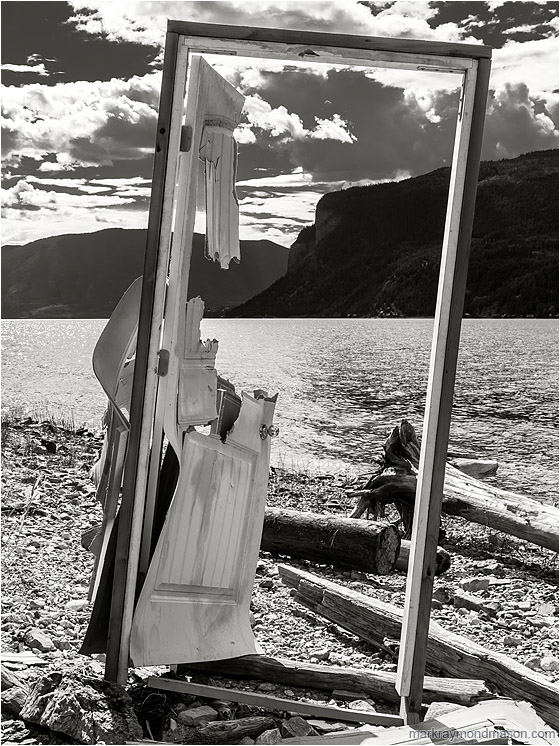 Door Frame, Rocky Beach: Shuswap Lake, BC, Canada (2016-07-10) - Fine art black and white photograph of a disembodied standing door with no walls and a beautiful background of lake, sky and mountains