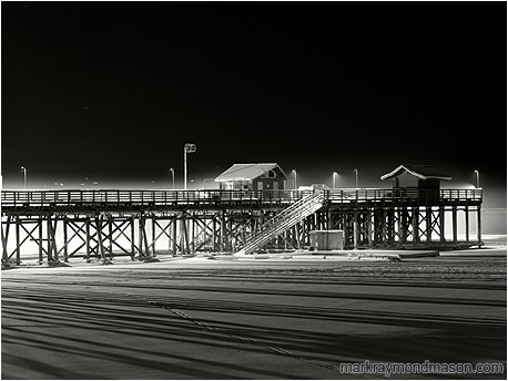 Fine art black and white photograph showing a thin shroud of fog around a lone snow-lined wharf on a black winter night