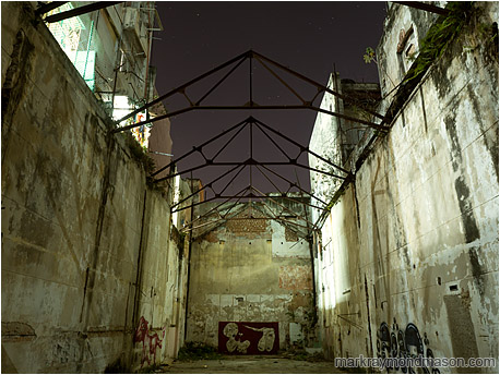 Fine art photograph showing a vacant urban canyon between concrete buildings, with exposed trusses against a starry sky