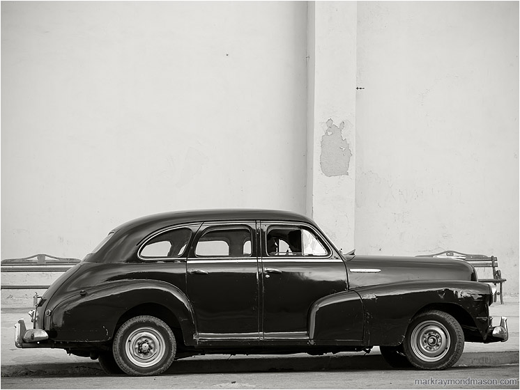 Parked Car, Silhouettes: Havana, Cuba (2017-02-15) - Fine art black and white photograph showing silhouetted lovers in a battered 1950s model car, parked beside a plain concrete wall