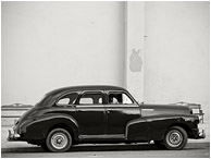 Parked Car, Silhouettes: Havana, Cuba (2017) - Fine art black and white photograph showing silhouetted lovers in a battered 1950s model car, parked beside a plain concrete wall