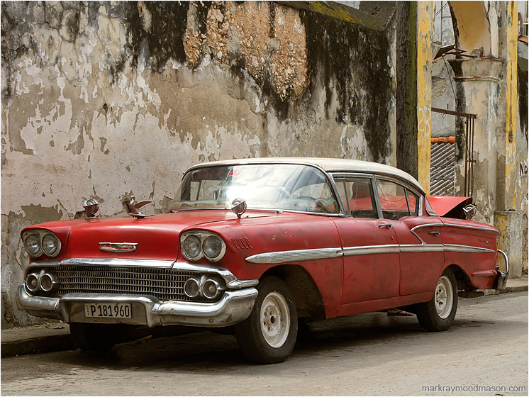 Red Car, Battered Wall: Casablanca, Cuba (2017-02-16) - Fine art photograph of a dingy 1950s era car in soft light, in front of a checked and stained concrete wall