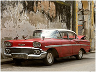 Red Car, Battered Wall: Casablanca, Cuba (2017) - Fine art photograph of a dingy 1950s era car in soft light, in front of a checked and stained concrete wall