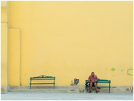 Coloured Wall, Man Reading: Havana, Cuba (2017) - Fine art travel photo of a man seated alone on a bench in front of a towering orange wall