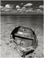 Battered Boat, Rolling Clouds: Near Vinales, Cuba (2017) - Fine art black and white photograph showing a flooded boat, cocked sideways, sitting abandoned on the silty shores of a shallow lake