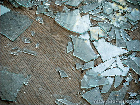 Fine art abstract photo showing shattered window glass and blurry reflections of fall colours on a bare, grainy plywood floor