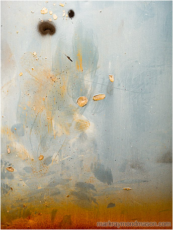Abstract fine art photo of burnt orange paint leaping upward like flames on a charred and scratched shop door
