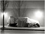 Street Shelter, Sleeping Figure: Vancouver, BC, Canada (2018) - Black and white photograph of a homeless person sleeping in a crude tarp and cardboard shelter against a tile wall