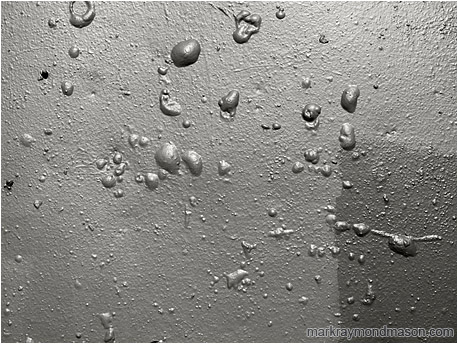 Black and white abstract photograph showing a pattern of bubbles on a crudely painted concrete wall